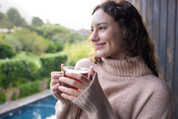 Smiling woman holding cup of tea, relaxing at home with scenic view