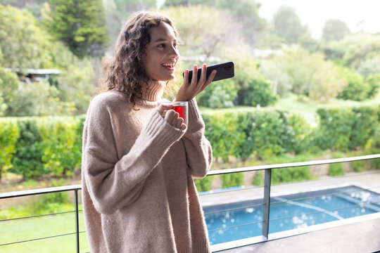 Holding smartphone and coffee cup, woman talking and relaxing on balcony, copy space