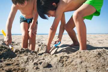 Brothers in swimming trunks dig a hole in the sand with toy shovels. © OR MIXphoto
