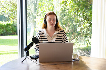 Using laptop and microphone, woman recording podcast at home office