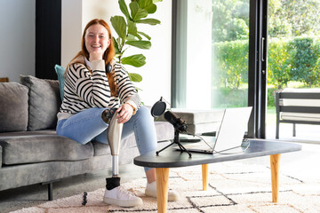 Sitting on couch, woman with prosthetic leg smiling, using laptop and microphone