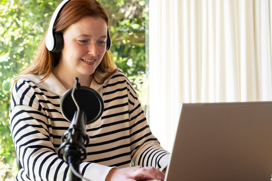 Using laptop and microphone, woman recording podcast while wearing headphones