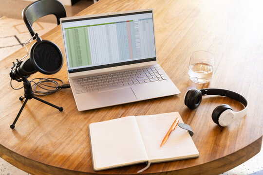 Podcasting setup with laptop, microphone, notebook, and headphones on wooden table, copy space