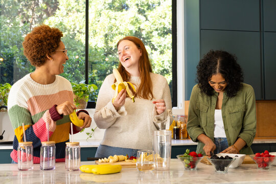 Preparing smoothies, diverse friends laughing and enjoying time together in kitchen