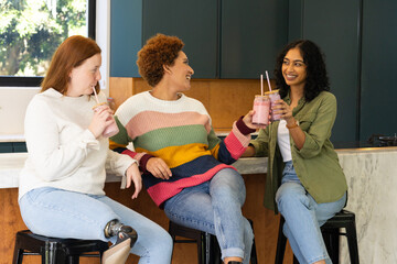 Drinking smoothies, diverse friends sitting and chatting in modern kitchen