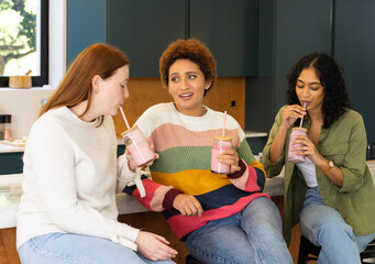 Drinking smoothies, diverse friends chatting and relaxing together in kitchen