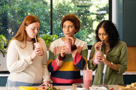 Drinking smoothies, diverse friends enjoying healthy drinks together in kitchen
