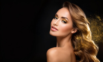 Fototapeta premium Beautiful model girl with golden makeup, hair on a black background, gold particles swirling like a comet wreck from hair on a black background