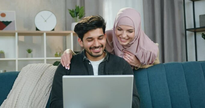 Man and woman planning their joint vacations while man uses computer and his girlfriend standing behind him and watching on computer screen