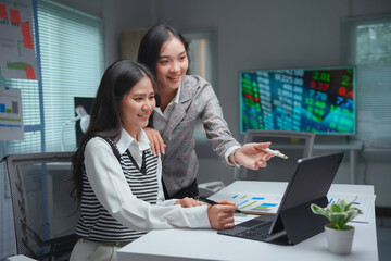 Two businesswomen are working together in the office analyzing stock market data on a laptop screen and discussing about investment strategy