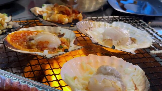 Scallops cooking on an open grill with different toppings in an outdoor food setting