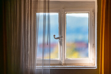 Old wooden window with white paint, historical shutter mechanism and blurred background. Yellowed curtains and drapes refract the incoming sunlight in the attic of a historic building. Idyllic scene.