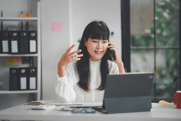 Young businesswoman is multitasking using laptop and talking on phone while working in her office