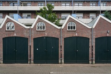 Row of brick garages with green doors and arched windows.