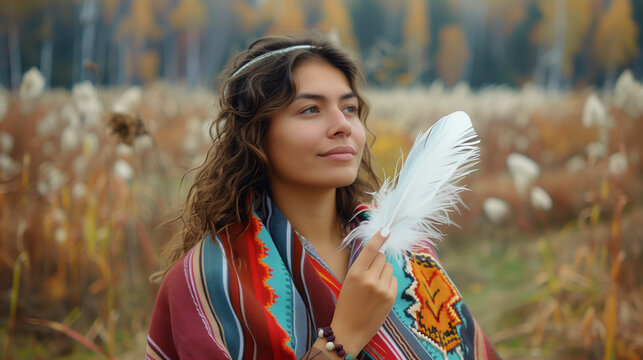 Young woman wearing colorful poncho holding white feather against the background of an autumn field