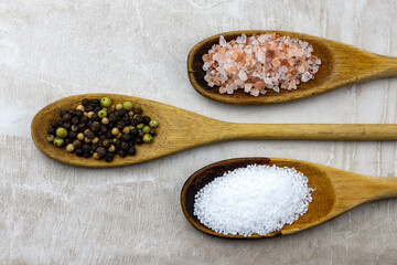 Three wooden spoons arranged on a neutral tile.  Spoons filled with pretzel salt, whole peppercorns, and himalayan salt.