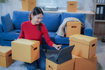 Freelance sme business owner is working on a tablet and holding a cardboard box to prepare products for delivery to customers