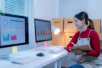 Asian woman happily works in a modern office, analyzing data for her business plan on a computer