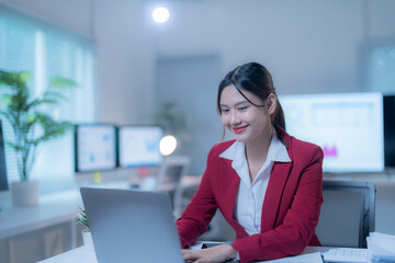 Obraz premium Focused asian businesswoman working late on laptop in dimly lit office, exuding confidence and professionalism. Captures essence of driven entrepreneur in modern workplace