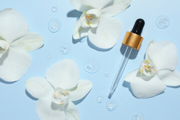 Beautiful orchid flowers and dropper with cosmetic product in water on light blue background, flat lay