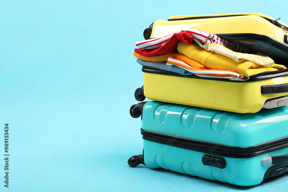 Poster Two suitcases with clothes on light blue background, space for text