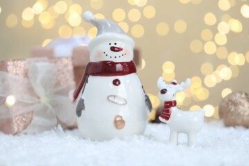 Funny snowman figure and decorative reindeer on artificial snow against blurred lights