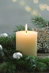 Burning candle, baubles and fir tree branches on wooden table, closeup