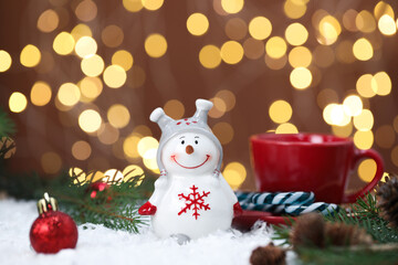 Funny snowman figure, cup and fir twigs on artificial snow against blurred lights