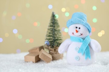 Cute snowman and small Christmas tree against beige background with blurred lights, bokeh effect