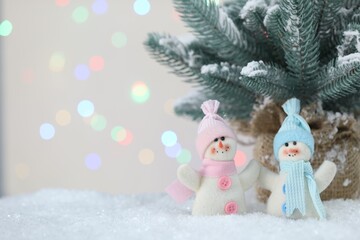 Cute snowmen and fir branches against beige background with blurred lights, bokeh effect. Space for text