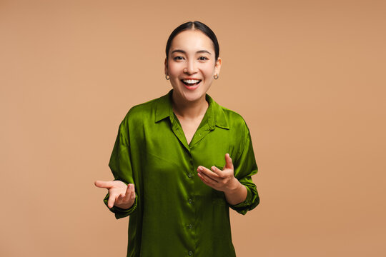 Positive, happy Asian woman wearing green shirt smiling, blogger recording video on beige background - Powered by Adobe
