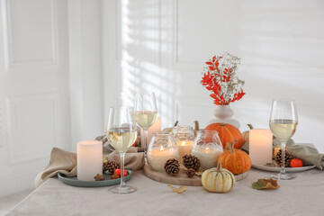 Autumn place setting with burning candles, glasses of wine and decor on table indoors