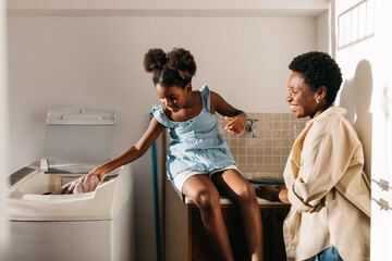 Happy mother and daughter washing clothes together at home