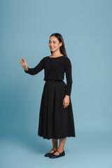 Smiling, Asian woman wearing black dress gesturing with hand on blue background