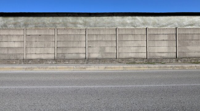 Concrete precast compound wall at the road side with fiberglass panel wall and sky on behind, cement sidewalk and street in front. Background for copy space.