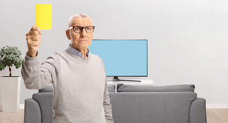 Serious elderly man showing a yellow card in front of tv