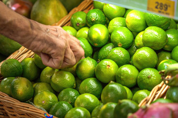Mature man picks fresh lime fruit in supermarket close-up.