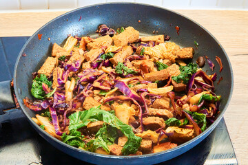 Colorful vegan stir fry with tofu, kale, cabbage, and carrots in a hot pan. A healthy and nutritious dish, full of vibrant vegetables and plant-based protein.