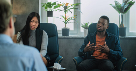 Multiethnic couple on consultation with psychologist. Irritated African American boyfriend talks...