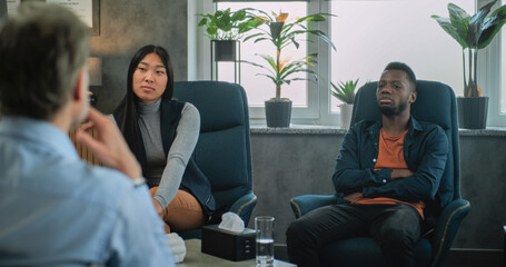 Back view of unfocused psychologist talking to young family during couples therapy. African American young man discusses relationship problems. Multiethnic couple on counseling session with therapist.