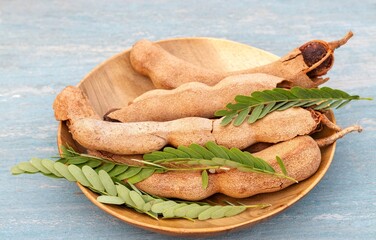 Closeup of Ripe Tamarind or Imli Fruit Heap with Leaves in a Wooden Bowl Isolated on Wooden Background