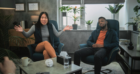 Obraz premium Back view of therapist conducting counseling session to multiethnic young family. Aggressive African American man loses temper, yells at his Asian girlfriend and starts fight during couples therapy.