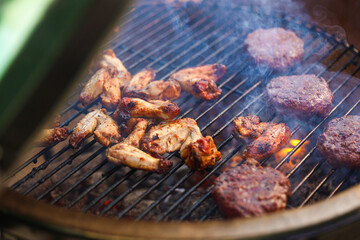 Barbecue concept photo. Charcoal ceramic grill full with chicken wings and meat for burgers. Cooking outside. Grill photo.  