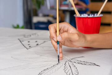 Close-up hand holding paintbrush while painting abstract on canvas for art, craft, with a red cup....