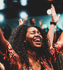 African American woman worshipping God in her church with her eyes closed and her arms in the air in praise