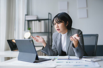 Young asian businesswoman is gesturing with hands while having a stressful video call on tablet in her office