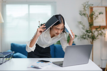 Young asian businesswoman is holding documents and screaming at her laptop with a frustrated expression