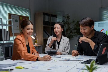 Team of asian businesspeople are working late in the office, smiling and discussing over paperwork
