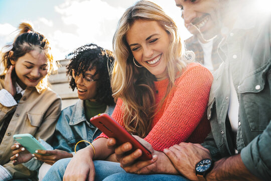 Group of young people using smart mobile phone outdoors - Happy friends with smartphone laughing together watching funny video on social media platform - Tech and modern life style concept