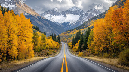 Winding road through an autumn forest lined with golden aspen trees leading to snow-capped mountains under dramatic cloudy skies, capturing the beauty of fall and nature's journey